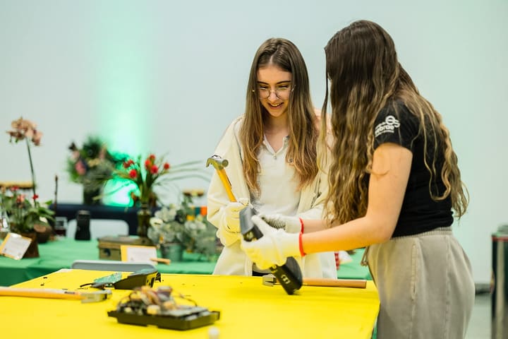 Duas participantes de luvas desmontam um disco rígido com martelo na oficina.